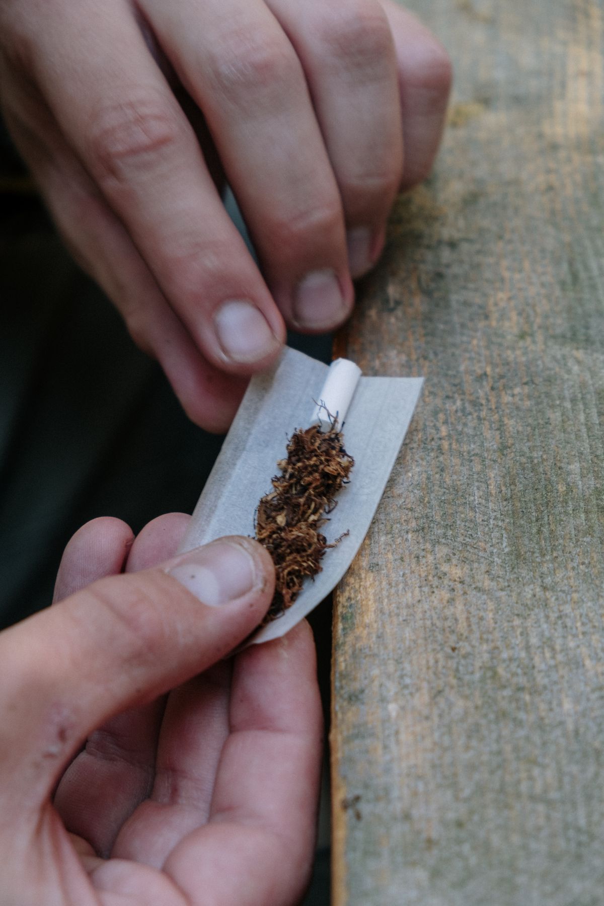 Ruce balící cigaretu, detail na tabák a papírek